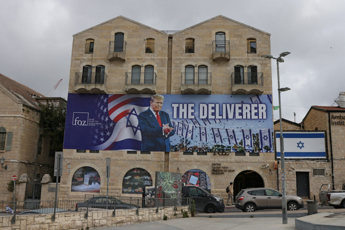 A photograph shows a banner depicting US President Donald Trump with the slogan 